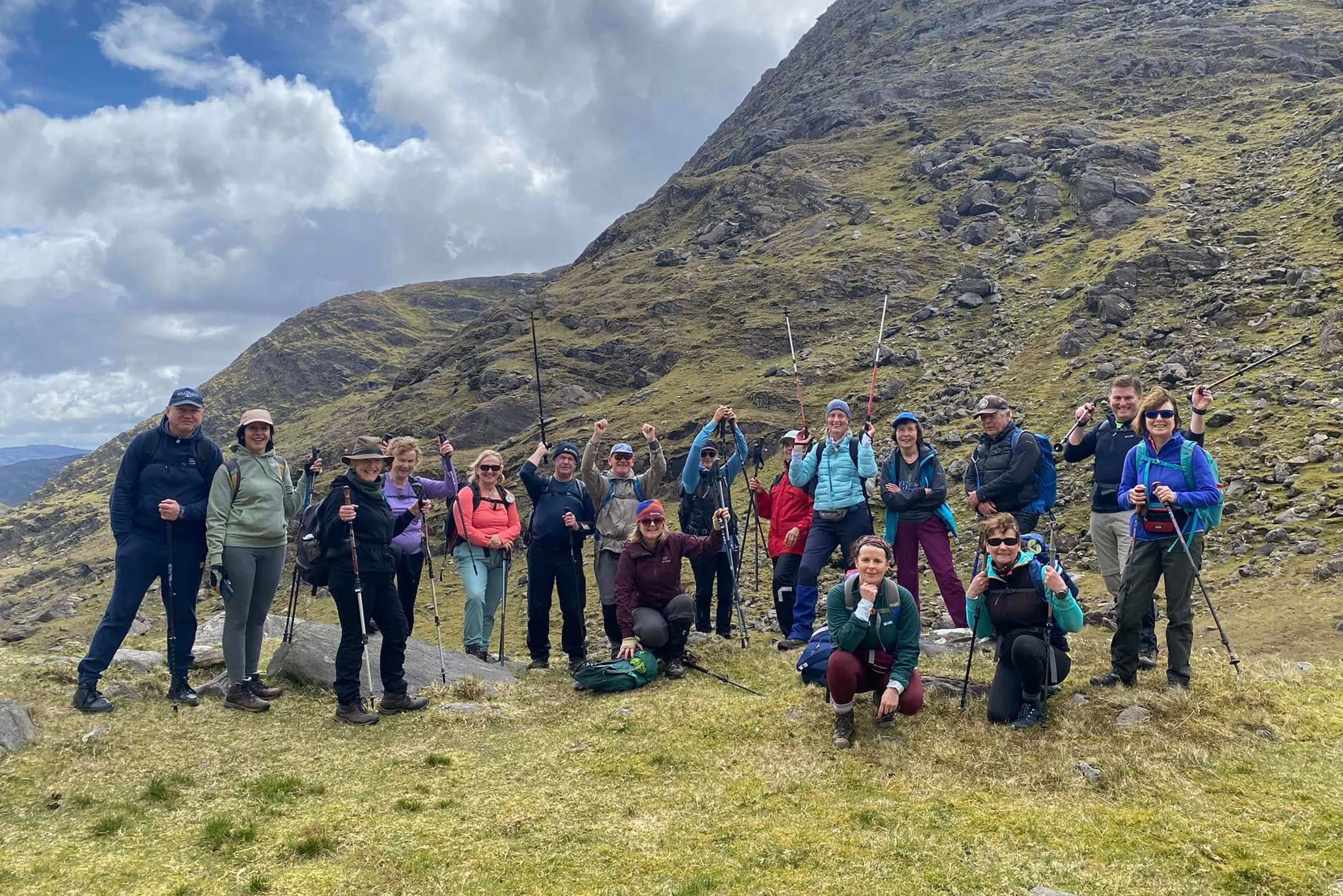 A large group of club members on a grassy hillside below a rocky ridge
