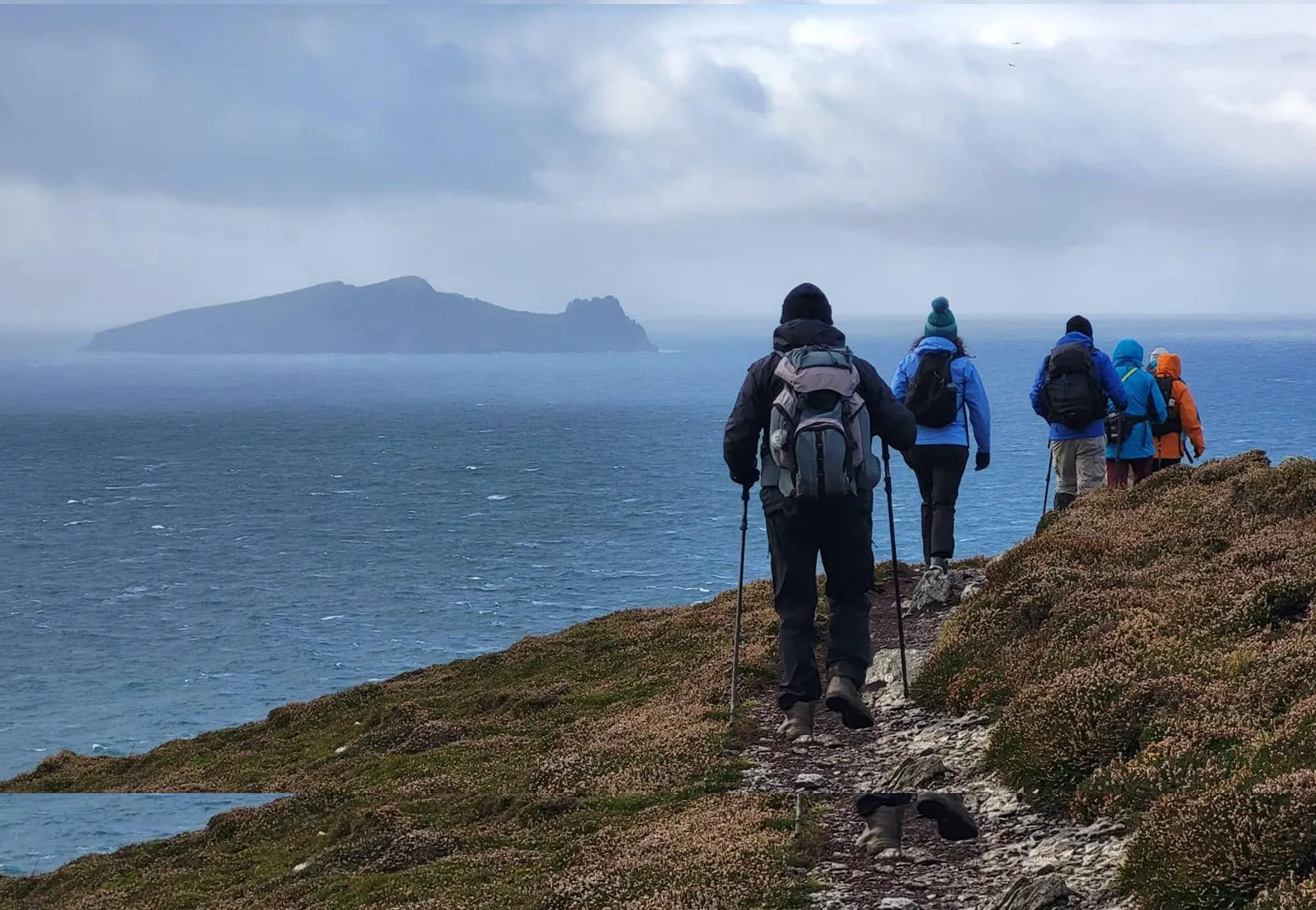 Club members hiking along a coastal path above the sea, with an island on the horizon